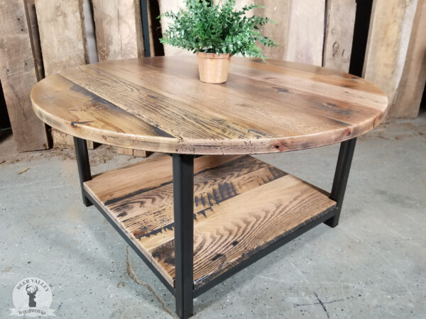 Rustic barnwood coffee table with thick round barnwood top and a lower shelf with blackened welded steel legs and framework.
