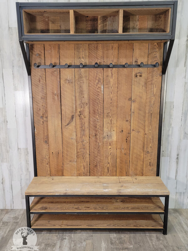 Rustic barnwood hall tree with a seating bench and two shelves, a full barnwood back with three cubbie compartments at the top, a row of repurposed railroad spike coat hooks and an antique blackened welded steel frame.