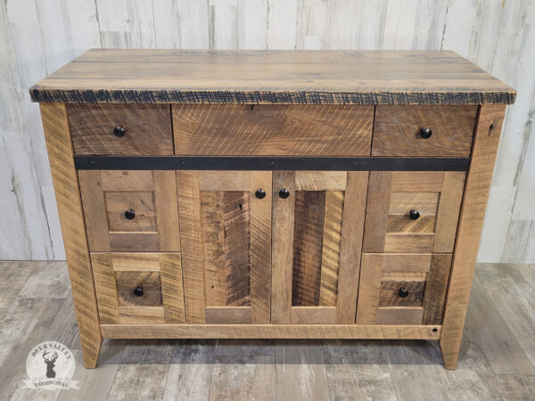 Barnwood farmhouse vanity with a large top, bank of three drawers on each side and center doors with recessed center panels with black drawer knobs and accented by antiqued blackened metal strap on the face.