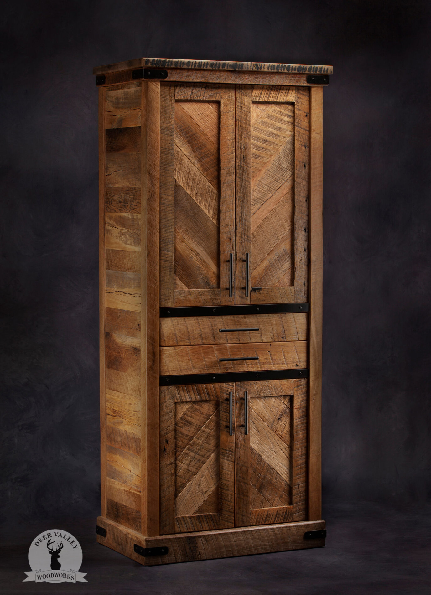 Farmhouse barnwood cupboard with chevron inspired pattern on the upper and lower doors separated by drawers and accented with a touch of blackened metal brackets and strapping.