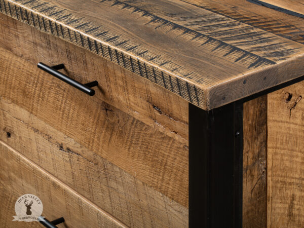 Closeup of the corner of a reclaimed wood corner desk showing the details in the barnwood and the black drawer pull.