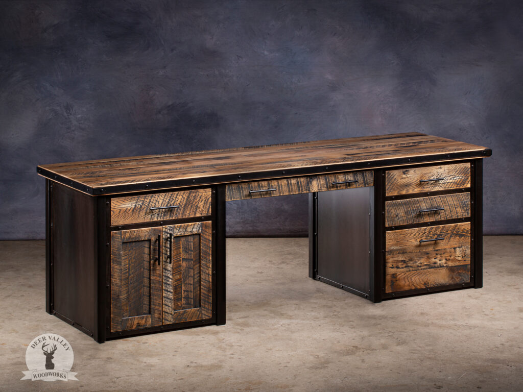 Industrial modern large executive office desk with reclaimed white oak lumber desktop wrapped in an antiqued steel strapping and secured with authentic welded steel rivets, a bank of three drawers on one end and a shallow drawer and pair of doors at the other end, a center flip-down pullout keyboard tray, blackened metal panels and blackened welded steel frame.
