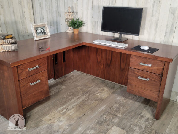 Modern black walnut corner desk with a Gunstock stain, large solid walnut top is supported by solid walnut side panels, each connected by a matching modesty panel, dual drawer banks at each end, with a standard drawer and a deep drawer.