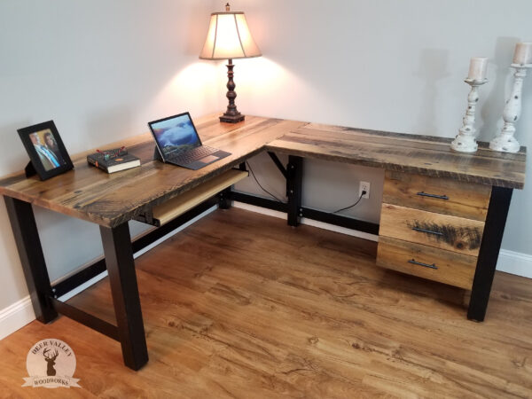 Rustic reclaimed wood three drawer corner desk with large desktop and blackened welded steel frame.