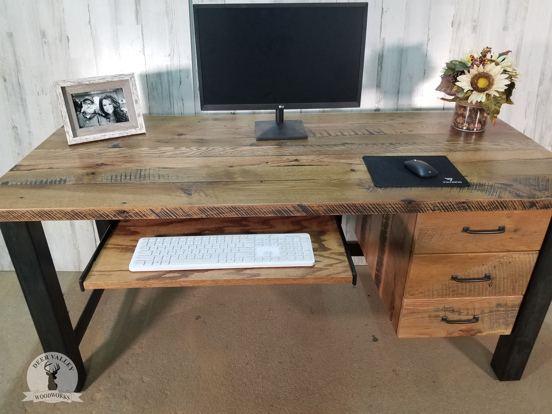 Rustic barnwood straight desk with a large desktop, pullout keyboard tray, three storage drawers, and an antiqued blackened welded steel frame.