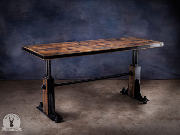 Industrial office desk with reclaimed white oak desktop wrapped in an antiqued steel strapping and secured with steel rivets, and blackened welded steel legs bolted to each other with steel threaded rod and bolts.