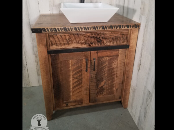 Farmhouse barnwood vanity with a barnwood top, barnwood doors with recessed center panels and antiqued blackened metal strap on the face and outside corner brackets.
