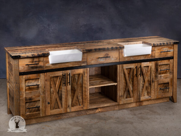 Rustic double sink barnwood vanity with large countertop and two handmade concrete farmhouse apron sinks, bank of three drawers at each end next to a set of double barnwood doors with recessed center panels, and centered between the sinks is a drawer with open shelving below, and antiqued blackened metal strap on the face and outside corner brackets.