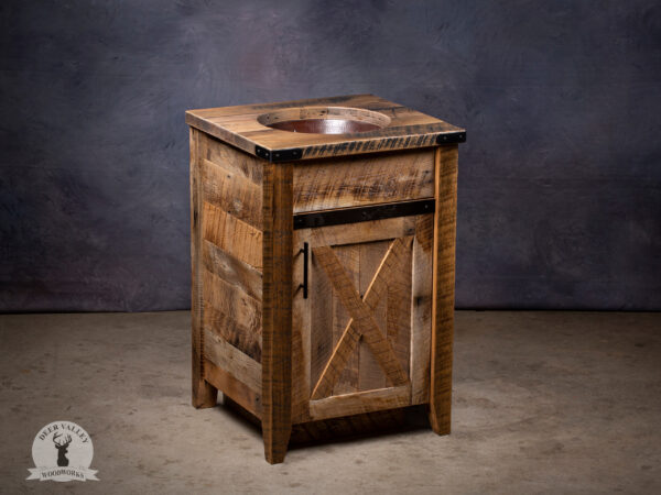Rustic barnwood vanity with a barnwood top, handmade copper sink with stars, and under the sink is a barnwood door with recessed center panel and antiqued blackened metal strap on the face and outside corner brackets.