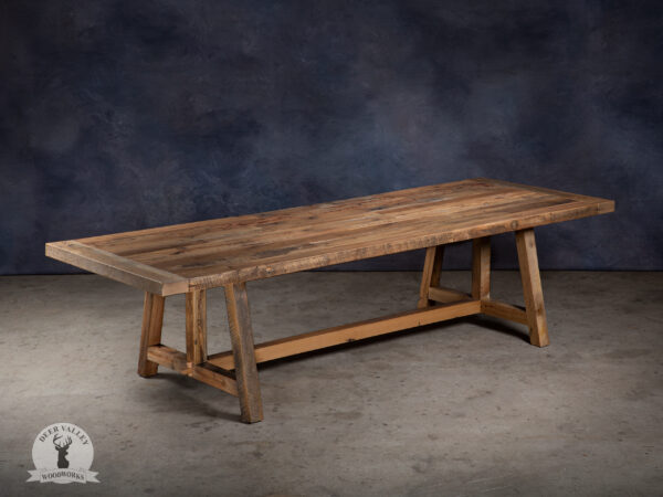 Farmhouse dining table handmade from reclaimed barnwood with a thick tabletop built with pinned mortise and tenon breadboard ends and wedged tenons that connect the table legs to each other.