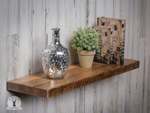 Custom made reclaimed barnwood floating shelf with glass vase, potted plant and book displayed on it.