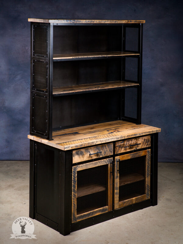 Industrial hutch with an upper section that has two blackened welded uprights with riveted metal mesh panels, solid barnwood shelves, and a blackened metal back panel and a lower section with two drawers and an shelves hidden behind a pair of barnwood doors with blackened mesh center panels, the sections are separated by a solid barnwood countertop. 