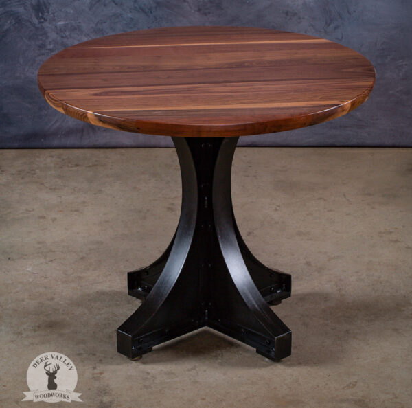 Industrial round table with a 1-1/2" thick walnut top and riveted rolled steel table legs with an antiqued blackened finish.
