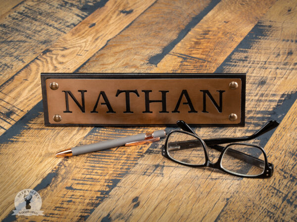 Industrial Name Plate fabricated from industrial steel, with a custom laser cut, and bronzed name plate, shown with the name Nathan and sitting on barnwood with a pair of glasses and a pen.