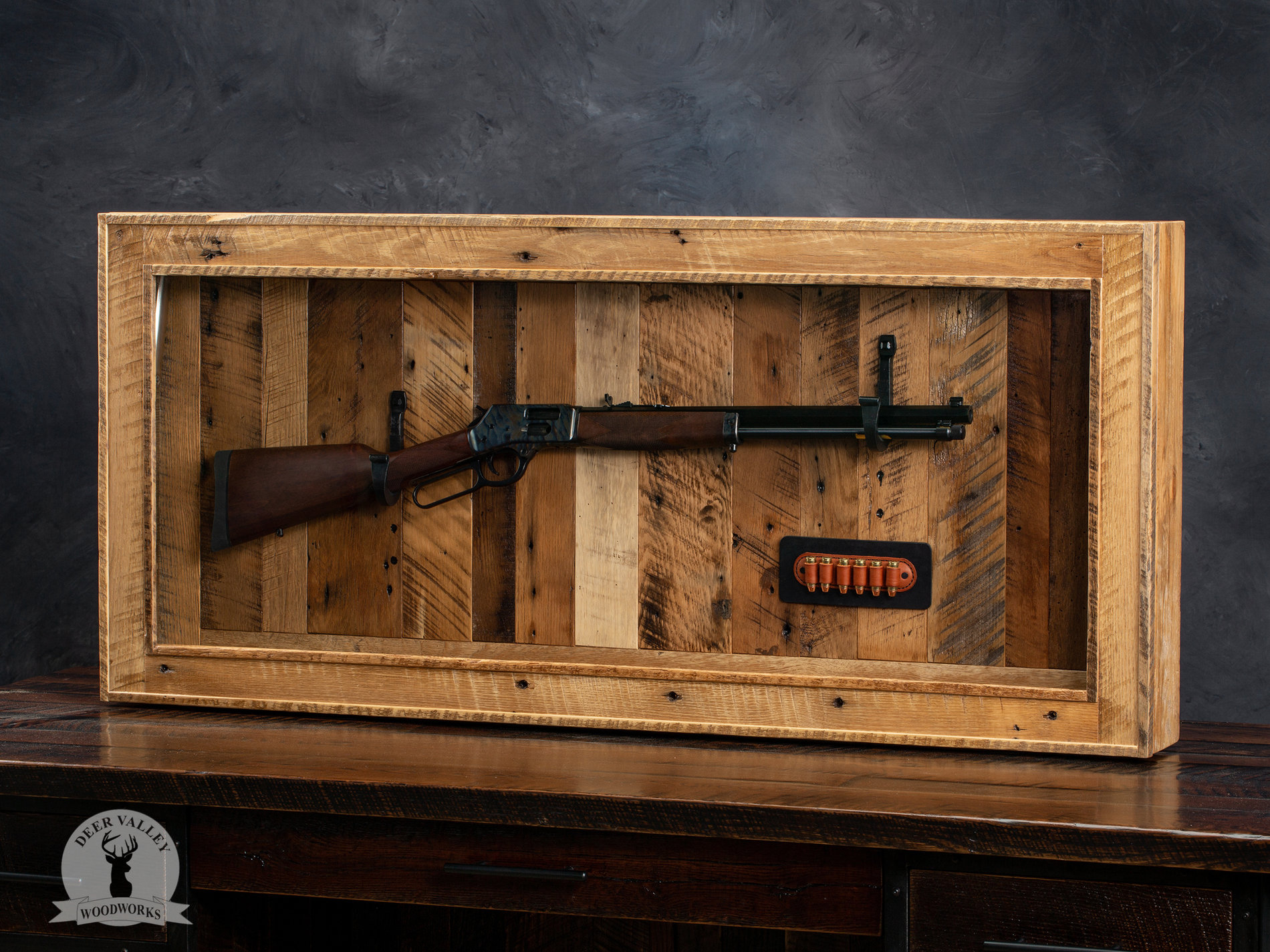 Authentic reclaimed barnwood gun case with a soft-close hinged door, museum anti-glare glass, and a skeleton key lock displaying a rifle on two forged steel hooks and a stitched leather bullet loop holder.